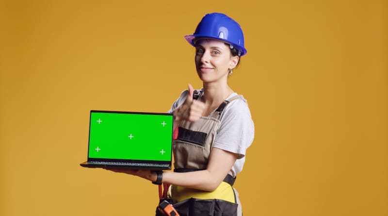 Foto feminina trabalhadora da construção civil segurando laptop com tela verde no estúdio, apontando para display chroma key com copyspace em branco. usando modelo de maquete isolado no computador, trabalhos de reparo.