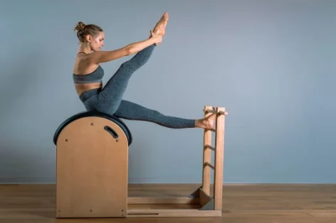 Foto linda mulher loira positiva realizando exercícios de pilates, treinando em equipamento de barril.