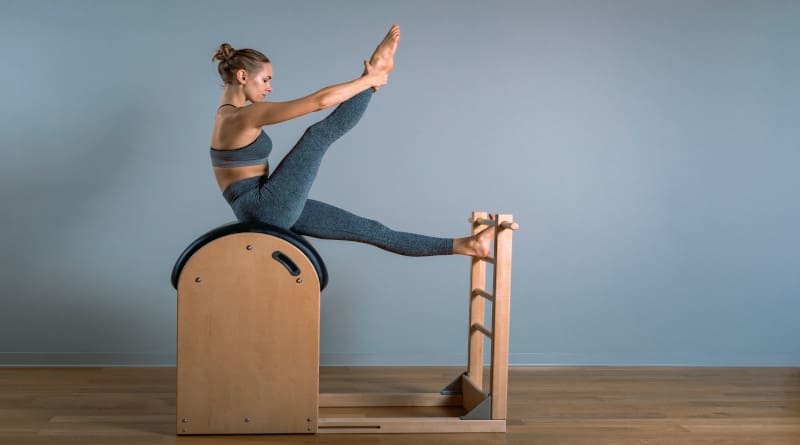 Foto linda mulher loira positiva realizando exercícios de pilates, treinando em equipamento de barril.