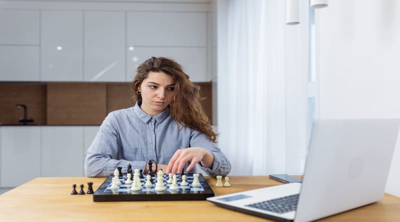 Foto linda garota sentada em casa jogando xadrez online com um laptop