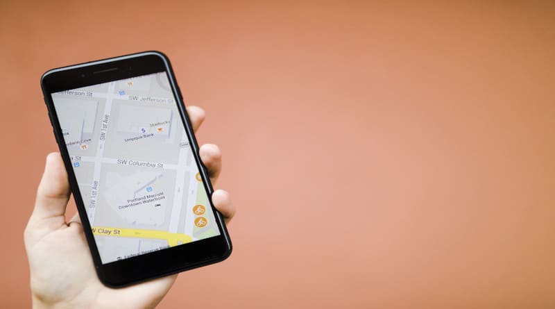 Foto de mão humana segurando um telefone celular com mapa de navegação GPS contra um fundo laranja