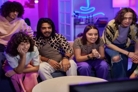 Foto de jovens interculturais amigáveis ​​em roupas casuais assistindo TV em festa em casa