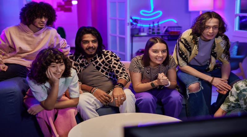 Foto de jovens interculturais amigáveis ​​em roupas casuais assistindo TV em festa em casa