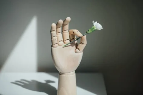 Close da foto de uma mão de madeira segurando flores brancas na mesa