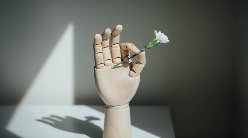Close da foto de uma mão de madeira segurando flores brancas na mesa