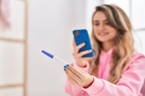 Foto jovem tira foto pelo smartphone para teste de gravidez no quarto