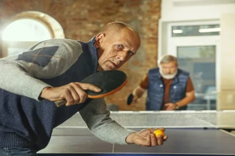 Foto de homens idosos jogando tênis de mesa no local de trabalho, se divertindo. amigos em roupas casuais jogam pingue-pongue juntos