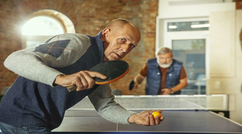 Foto de homens idosos jogando tênis de mesa no local de trabalho, se divertindo. amigos em roupas casuais jogam pingue-pongue juntos