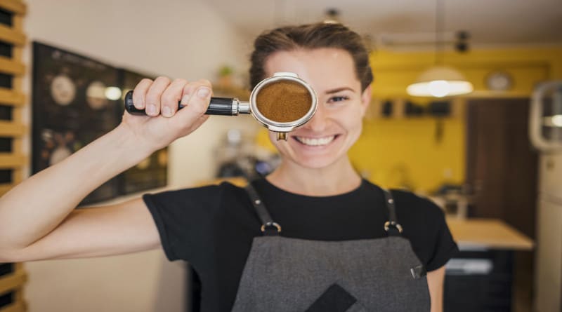 Foto vista frontal de uma barista feminina posando com uma xícara de máquina cheia de café