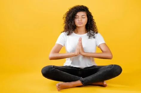Foto de mulher negra relaxada meditando em pose de ioga isolada sobre amarelo