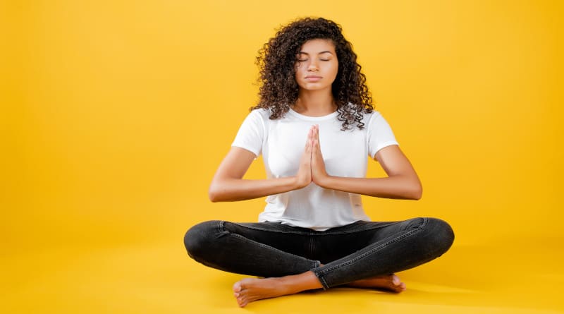 Foto de mulher negra relaxada meditando em pose de ioga isolada sobre amarelo