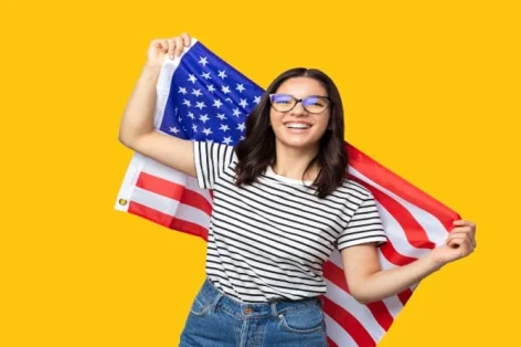 Foto jovem alegre, multietnia, feminina, segurando a bandeira americana contra um fundo amarelo