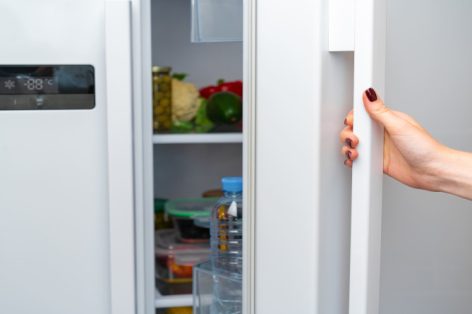 Foto de mão feminina abrindo a porta de uma geladeira de perto