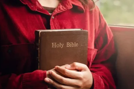 Uma adolescente vestindo uma camisa vermelha segura uma Bíblia Sagrada nos braços
