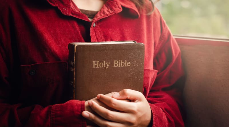 Uma adolescente vestindo uma camisa vermelha segura uma Bíblia Sagrada nos braços